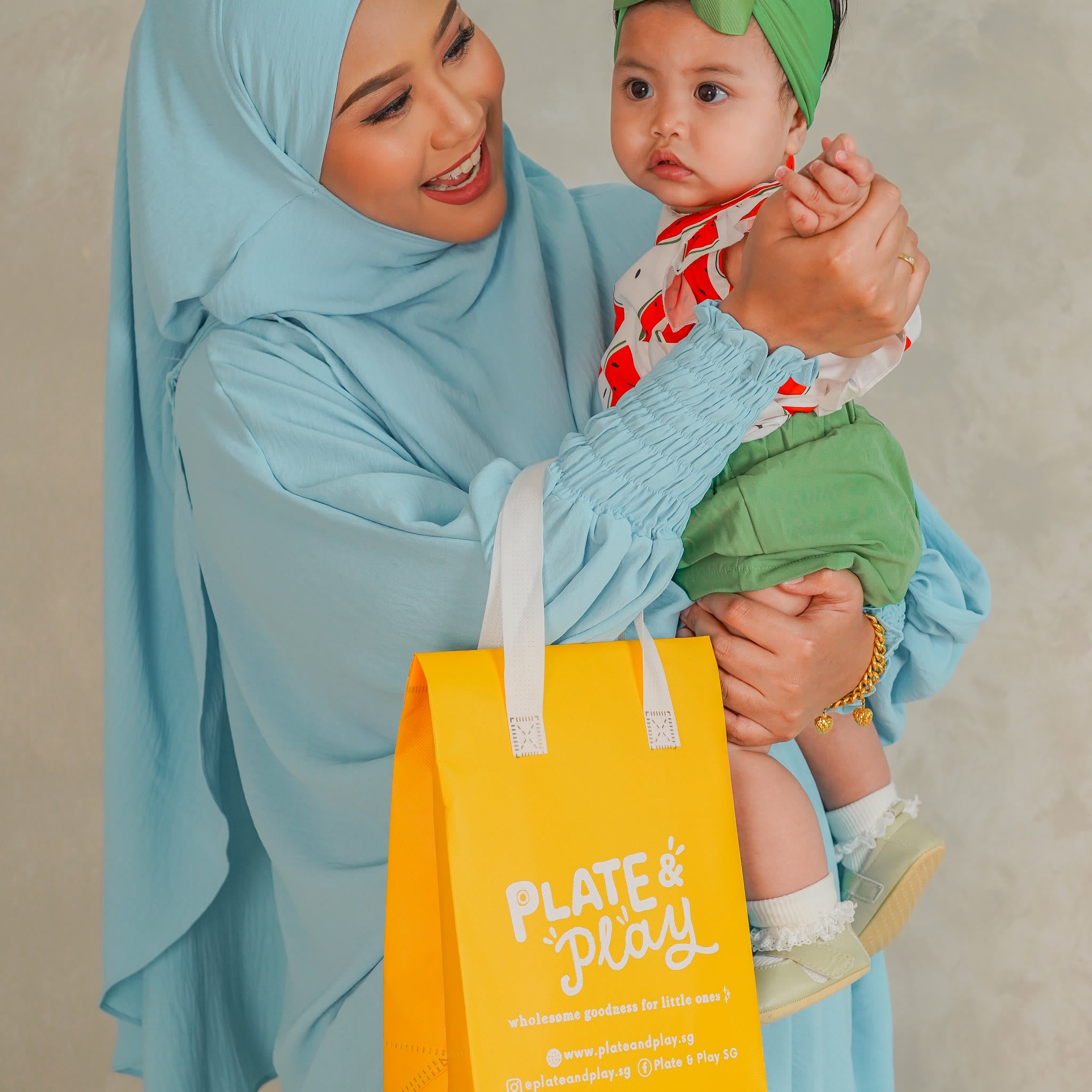 Mum holding her baby beside a yellow Plate and Play delivery bag