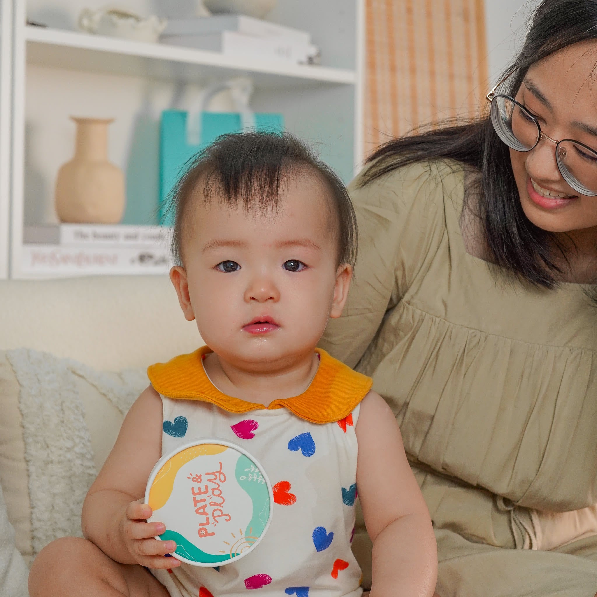 Baby holding a Plate and Play tub while sitting with her mum